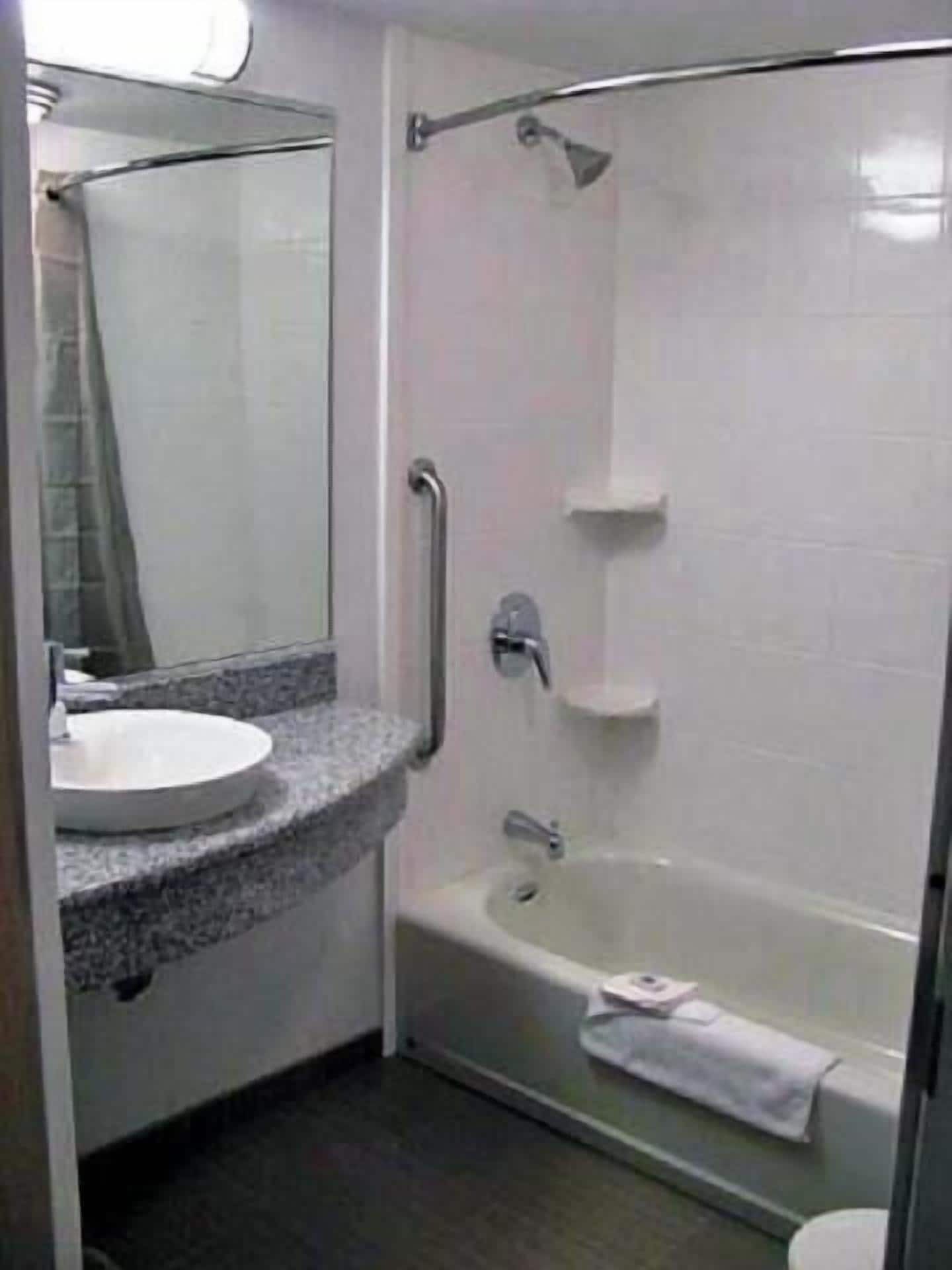 A bathroom with a sink, mirror, and a walk-in shower with a grab bar.