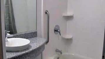 Un baño con lavamanos, espejo y cabina de ducha con barra de apoyo.