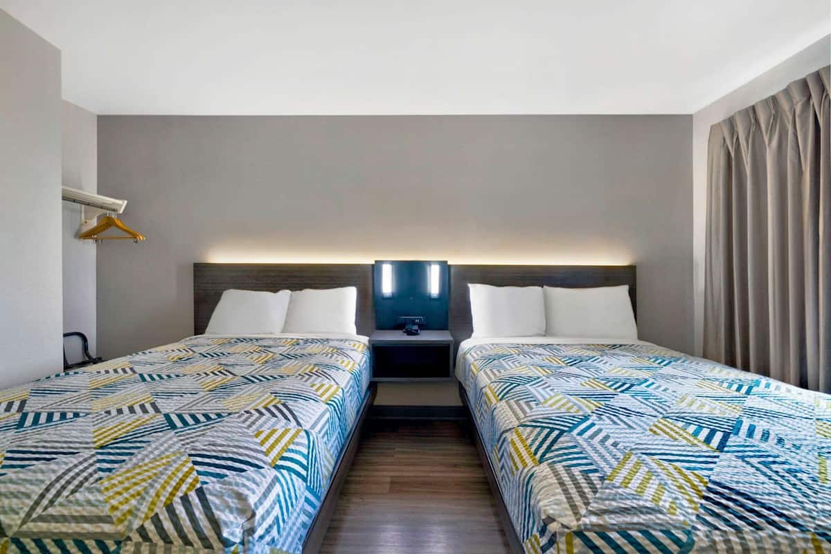 A hotel room with two beds, a nightstand, a wall-mounted TV, and a hanging coat rack.