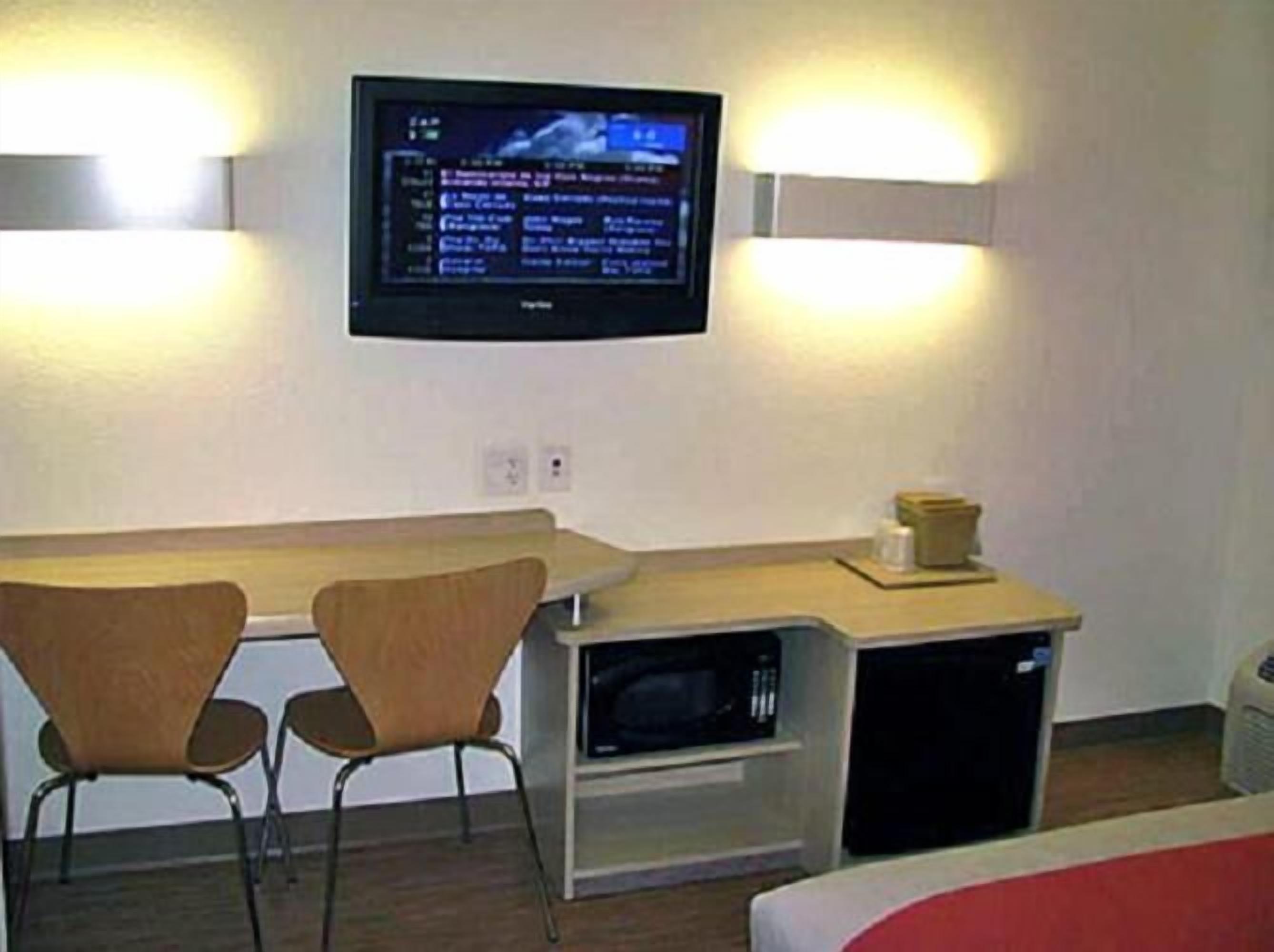 A small room with a desk, two chairs, a television mounted on the wall, and a microwave on the desk.