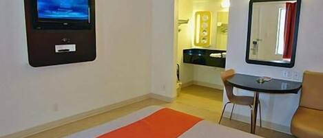 A hotel room with a bed, a TV mounted on the wall, a small table with a chair, and a mirror on the wall.