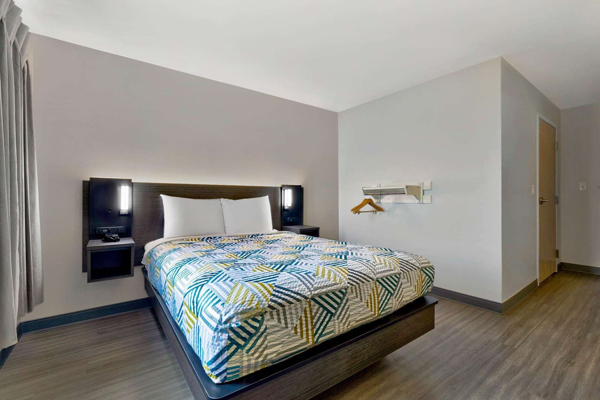 Una habitación de hotel con cama, mesitas de noche, televisor y perchero.