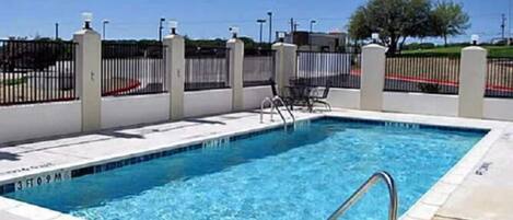 A rectangular swimming pool with a metal ladder, surrounded by a white tiled deck.