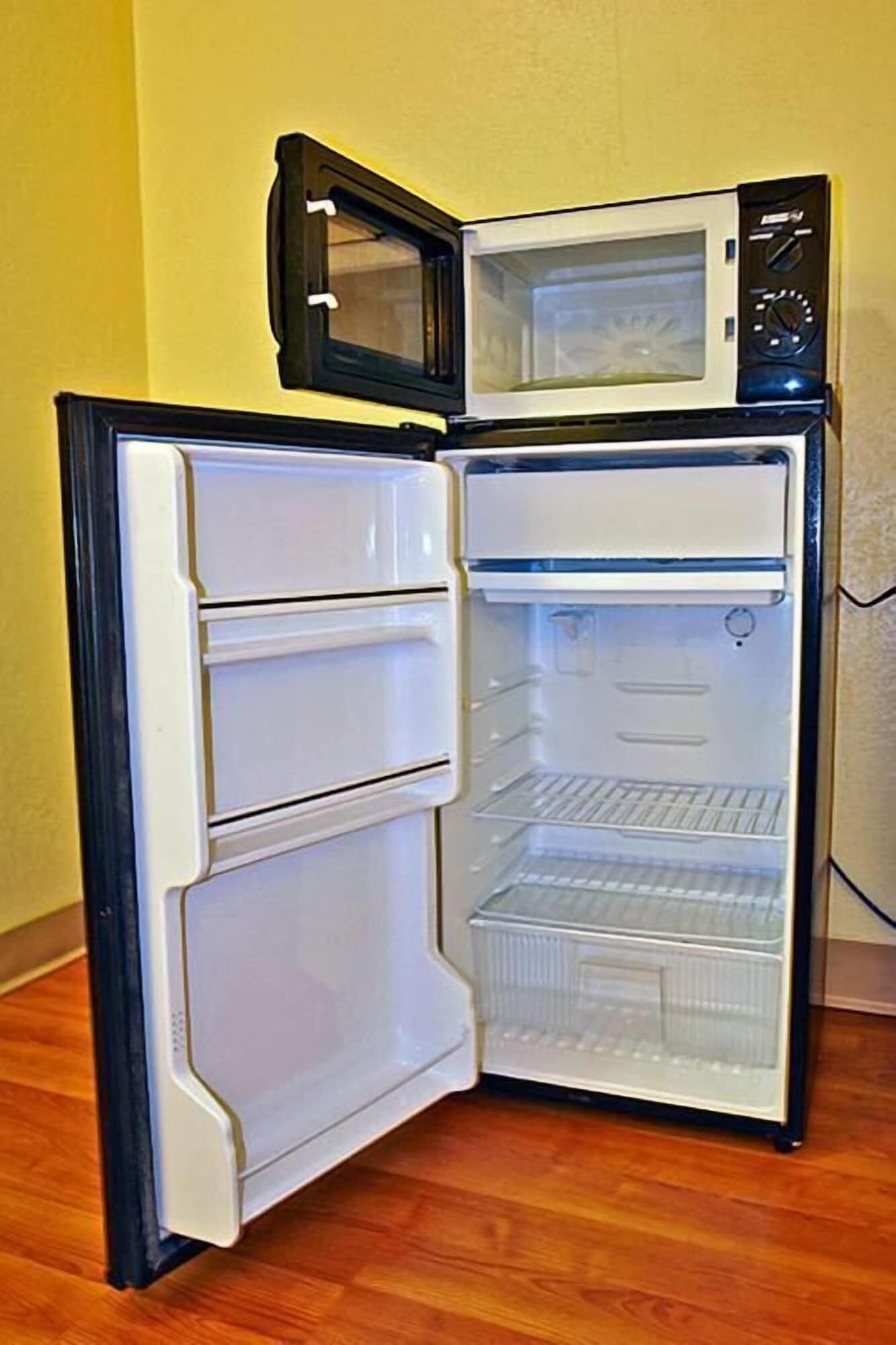 An open refrigerator with a microwave on top, a freezer compartment, and a shelf.
