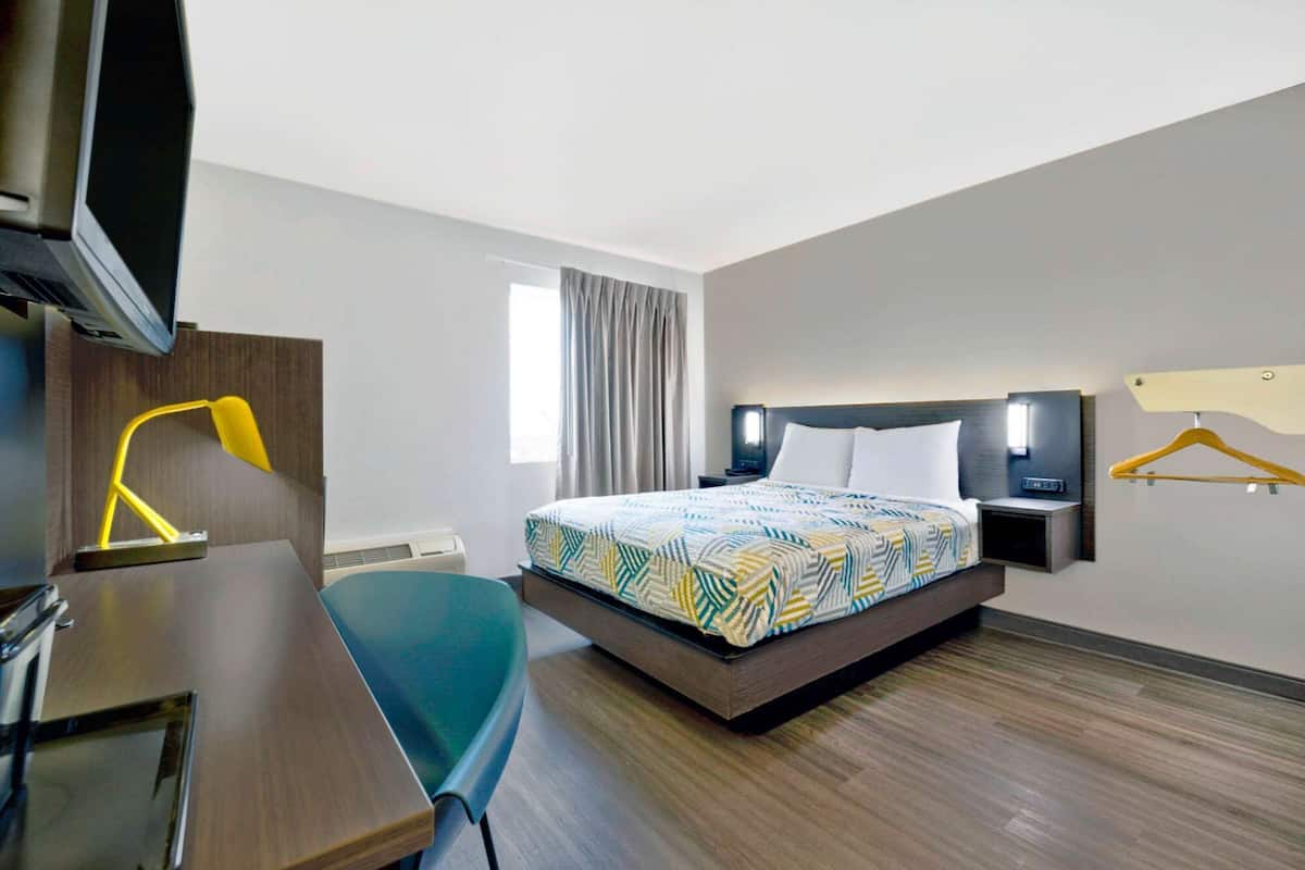 A hotel room with a bed, a desk, a chair, a TV, a lamp, and a window with curtains.