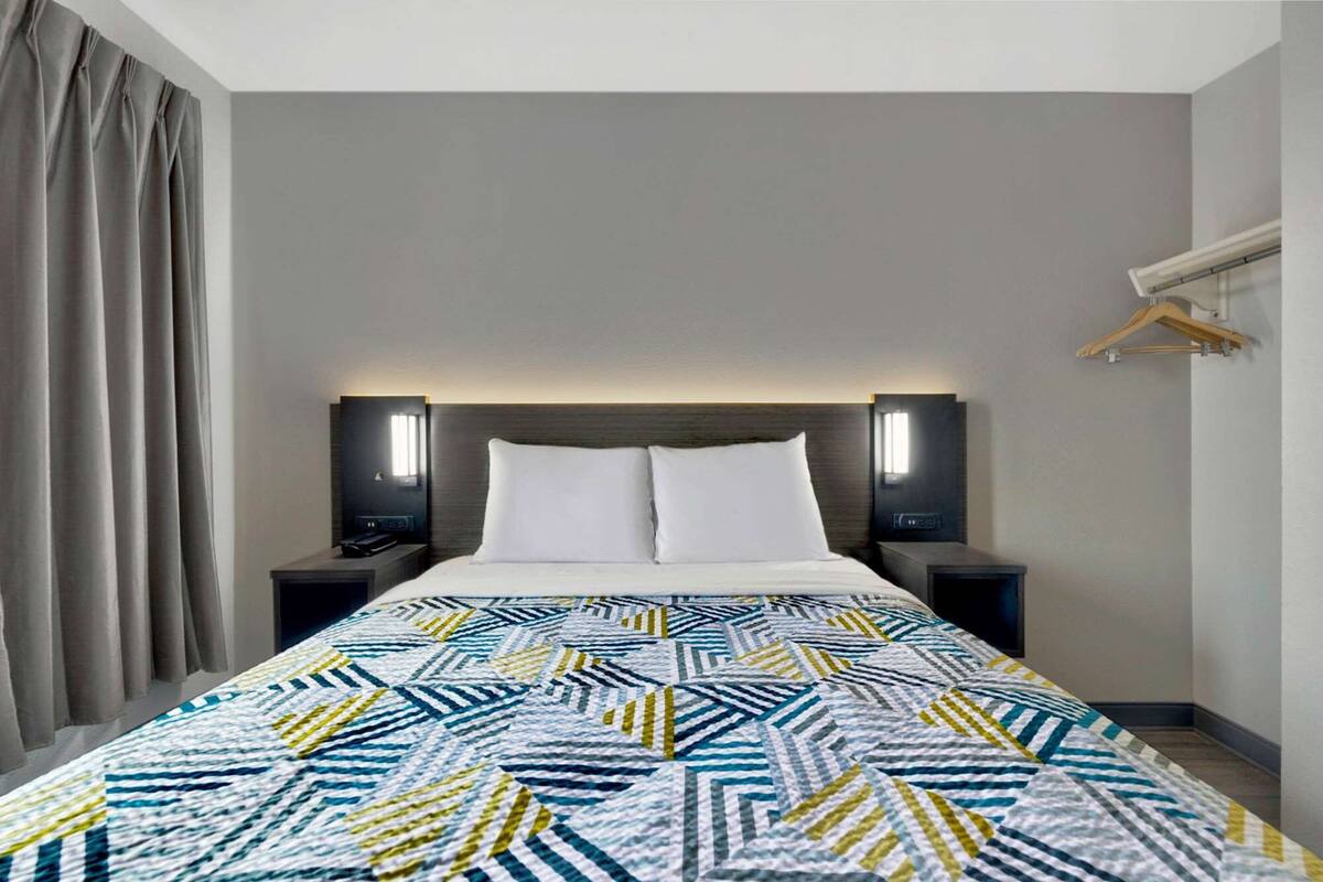 A hotel room with a bed, two bedside tables, a headboard, and a hanging clothes rack.