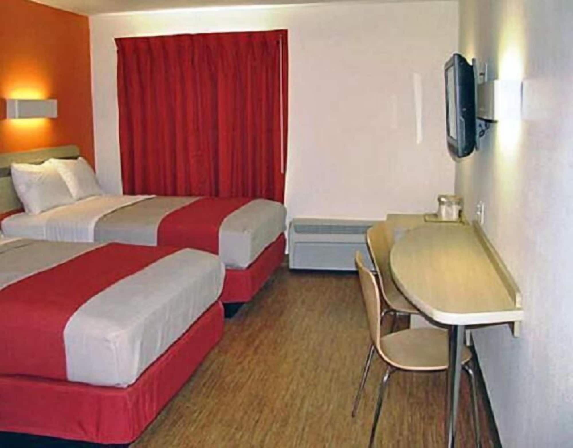 A hotel room with two beds, a desk, and a chair.