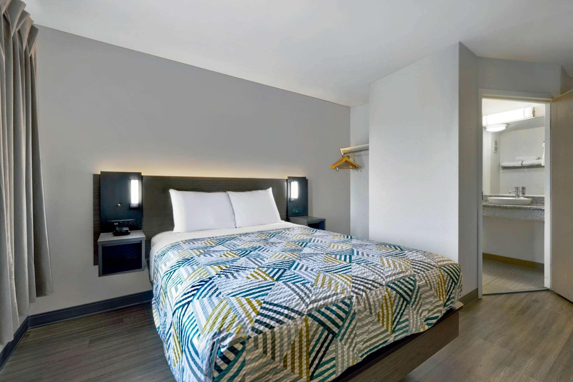 Une chambre d’hôtel avec un lit, des tables de chevet, une télévision, un radiateur fixé au mur et une salle de bain visible à travers une porte ouverte.