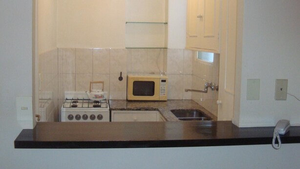 Una cocina compacta con estufa a gas, microondas y pileta.