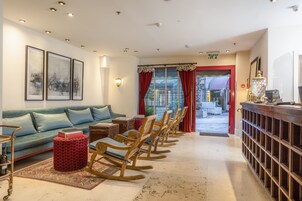 Un vestíbulo de hotel con un sofá azul, mecedoras de madera, un reposapiés rojo y una zona de bar.
