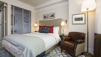 Habitación de hotel con una cama grande, un sillón de cuero marrón, una lámpara de pie y una mesita de noche con lámpara.