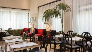 A dining area with tables and chairs, a red sofa, and a large plant.