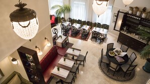 Un comedor amplio con varias mesas y sillas, un sofá rojo y una planta grande en maceta.