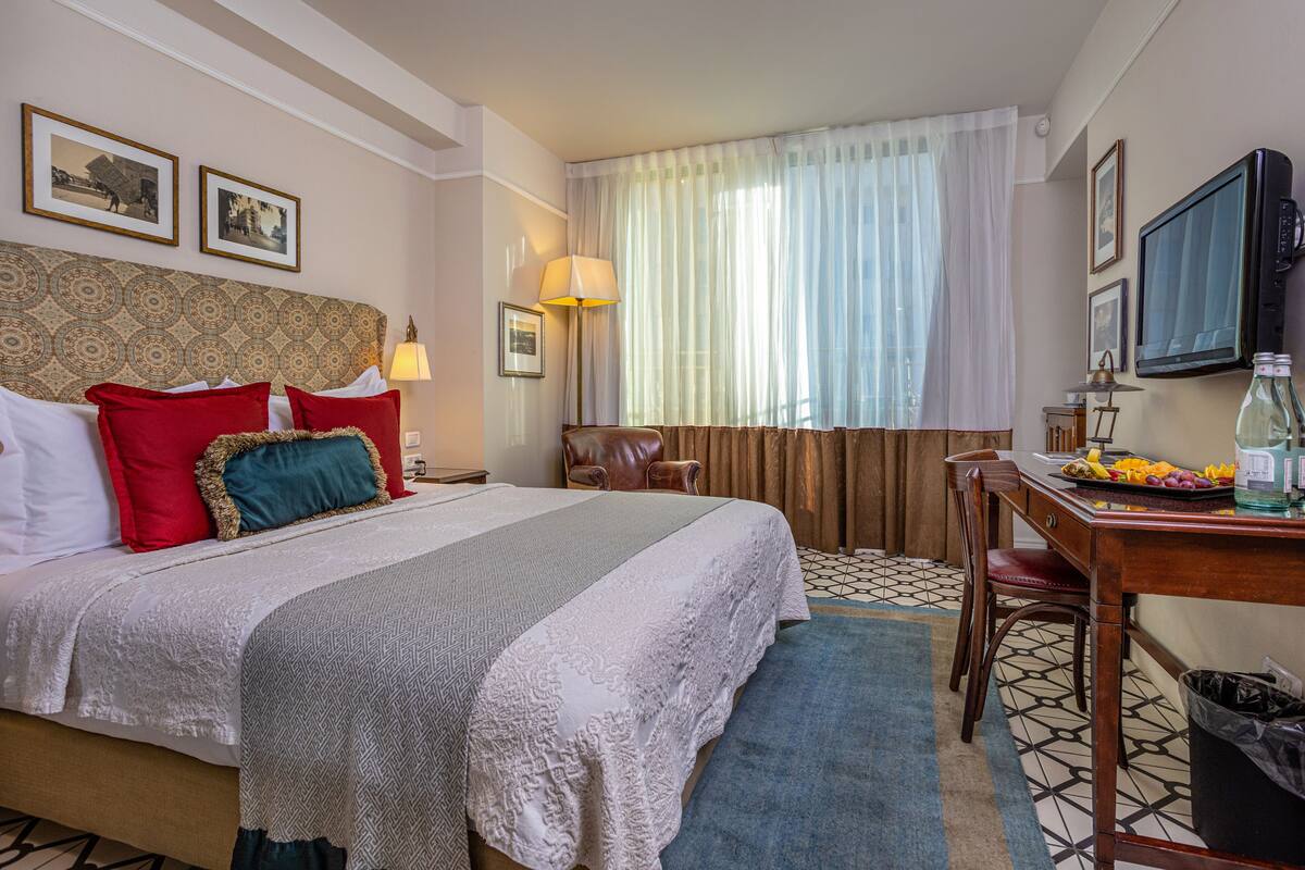 A hotel room with a large bed, a desk with a chair, a television, and a window with curtains.