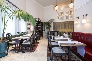Un área de comedor con mesas y sillas, un sofá rojo y una planta grande en maceta.