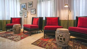Una habitación con cuatro sillones tapizados en rojo, un rug adornado con motivos y un taburete decorativo.