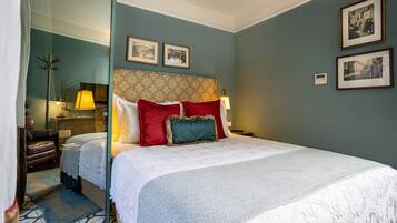 Une chambre d’hôtel bien aménagée, avec un grand lit, un coin salon comprenant une chaise et une table, et un miroir qui reflète la pièce.