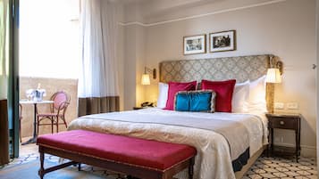 Habitación de hotel con una cama grande, un banco, una mesita y una silla.