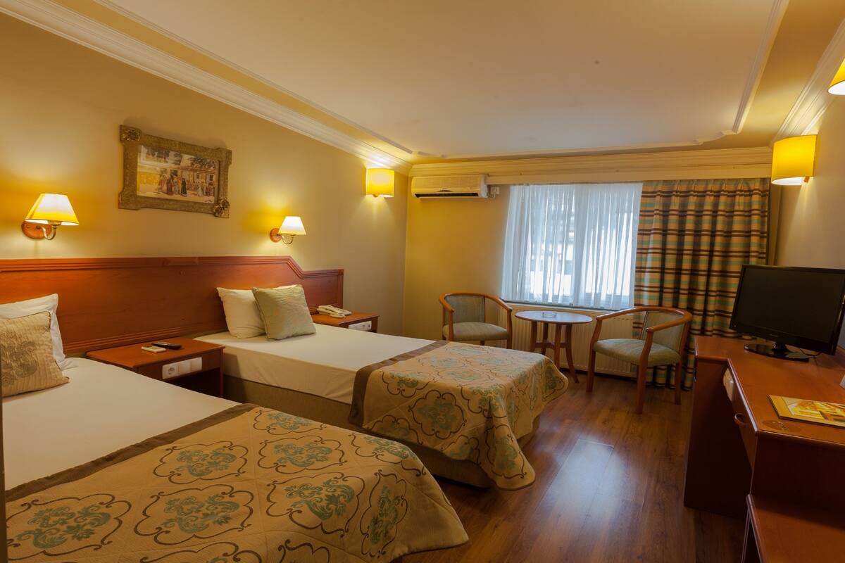 Hotelkamer met twee bedden, een bureau, een stoel, een televisie en een raam met gordijnen.