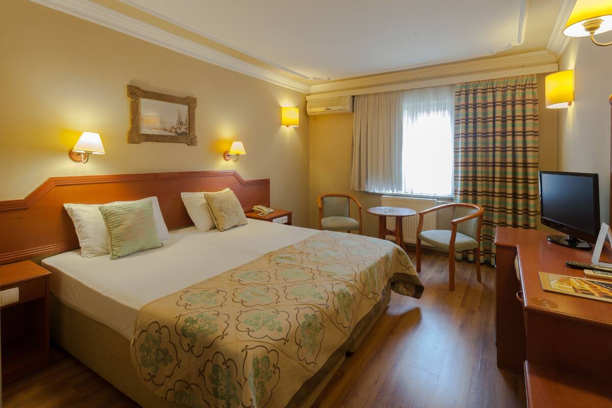 Hotelkamer met een groot bed, nachtkastjes, een bureau met stoel, een televisie en een raam met gordijnen.