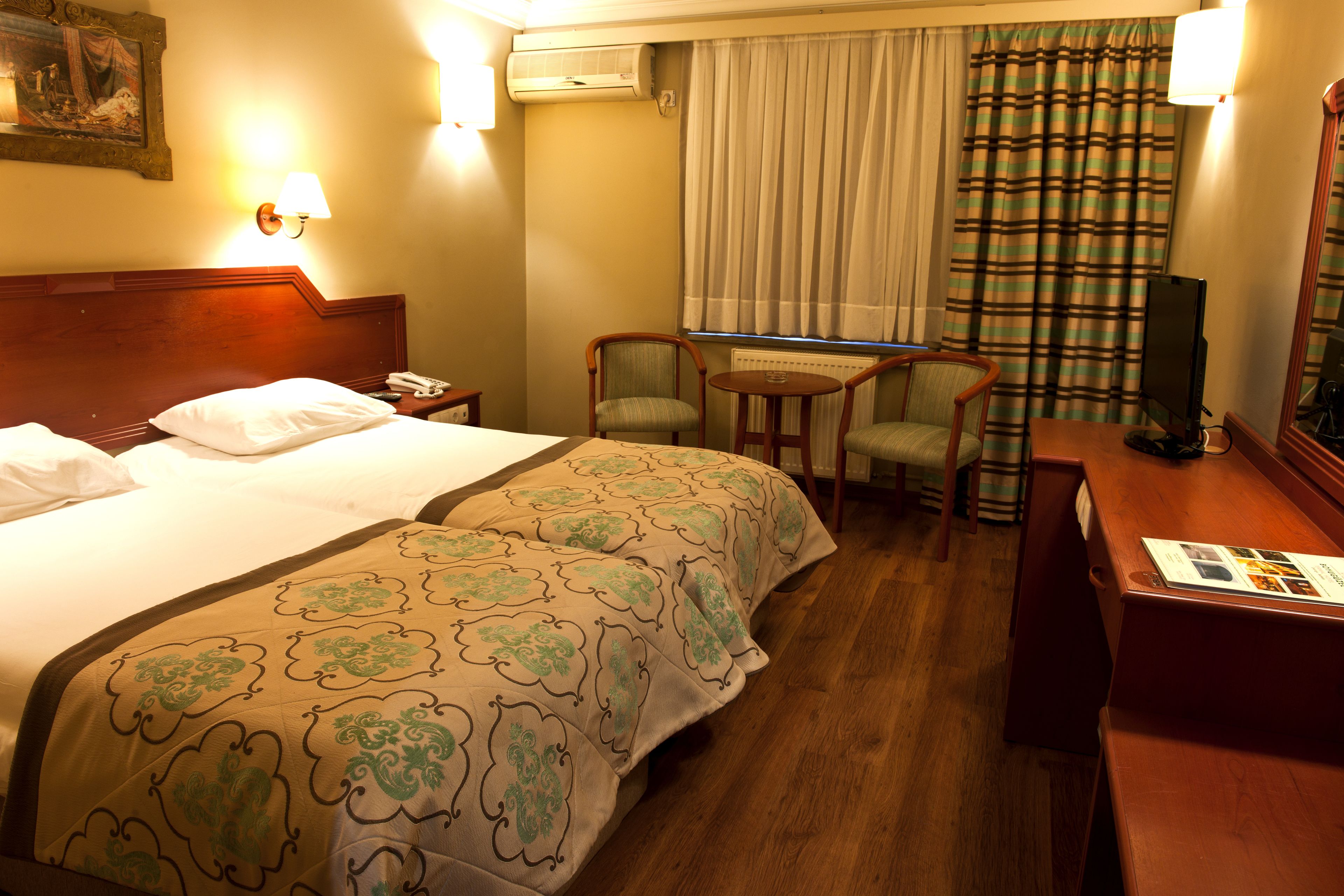 Habitación de hotel con dos camas, un escritorio, una silla, una lámpara y una ventana con cortinas.