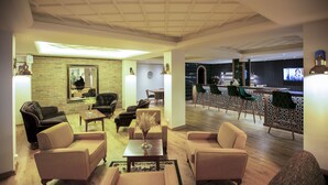 Amplio salón con varios sofás, una mesa de centro, pared de ladrillo y una zona de bar con sillas verdes.