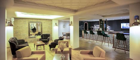 A spacious living area with multiple sofas and a coffee table, a brick wall, and a bar area with green chairs.