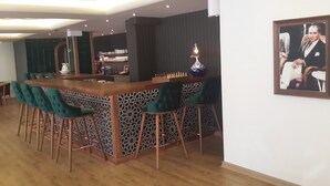 Un área de bar moderna con mostrador de madera, taburetes de bar tapizados en verde y una pared con diseño.
