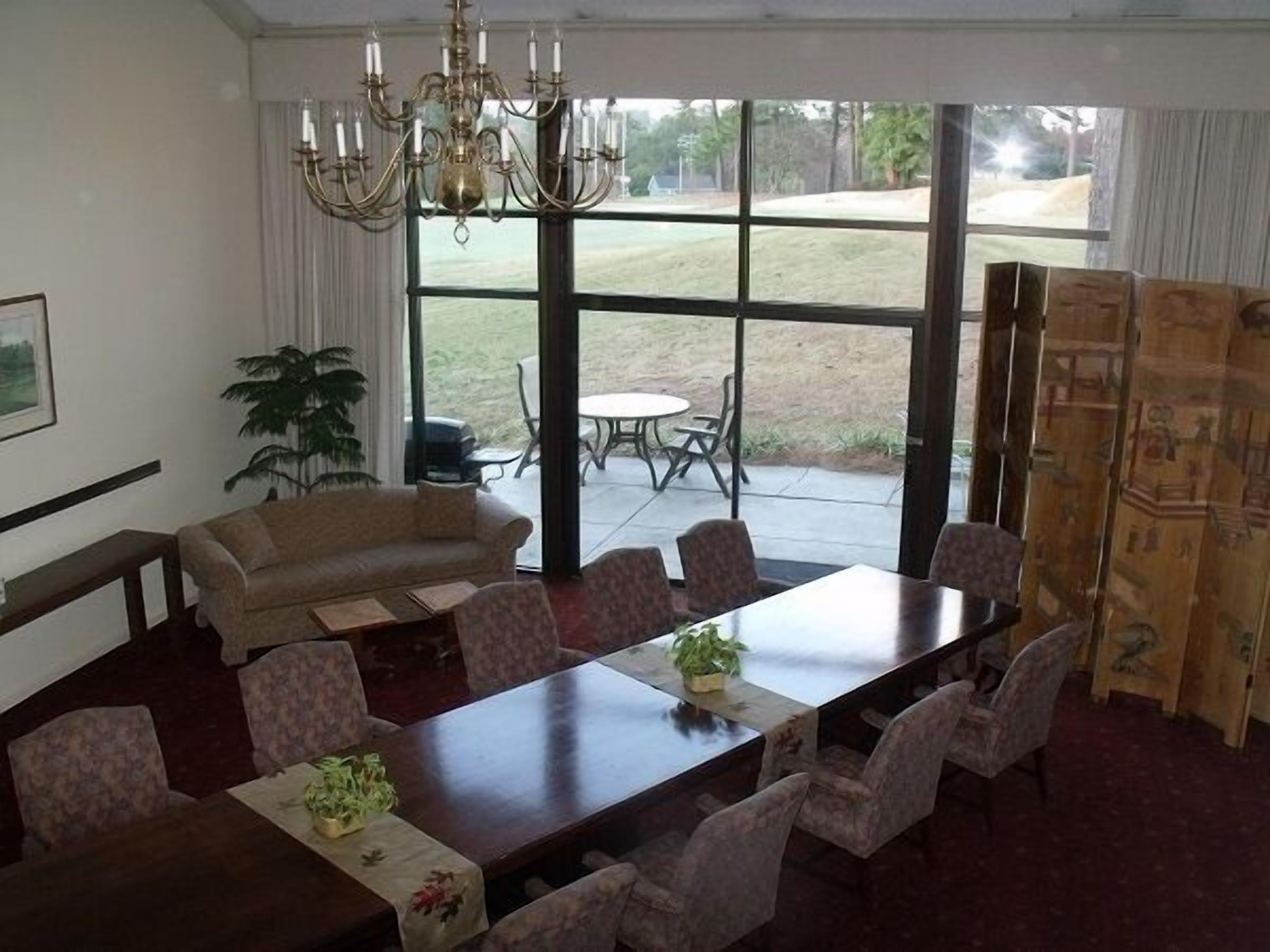 A dining area with a large table, floral-patterned chairs, a chandelier, and a view of the outdoors.