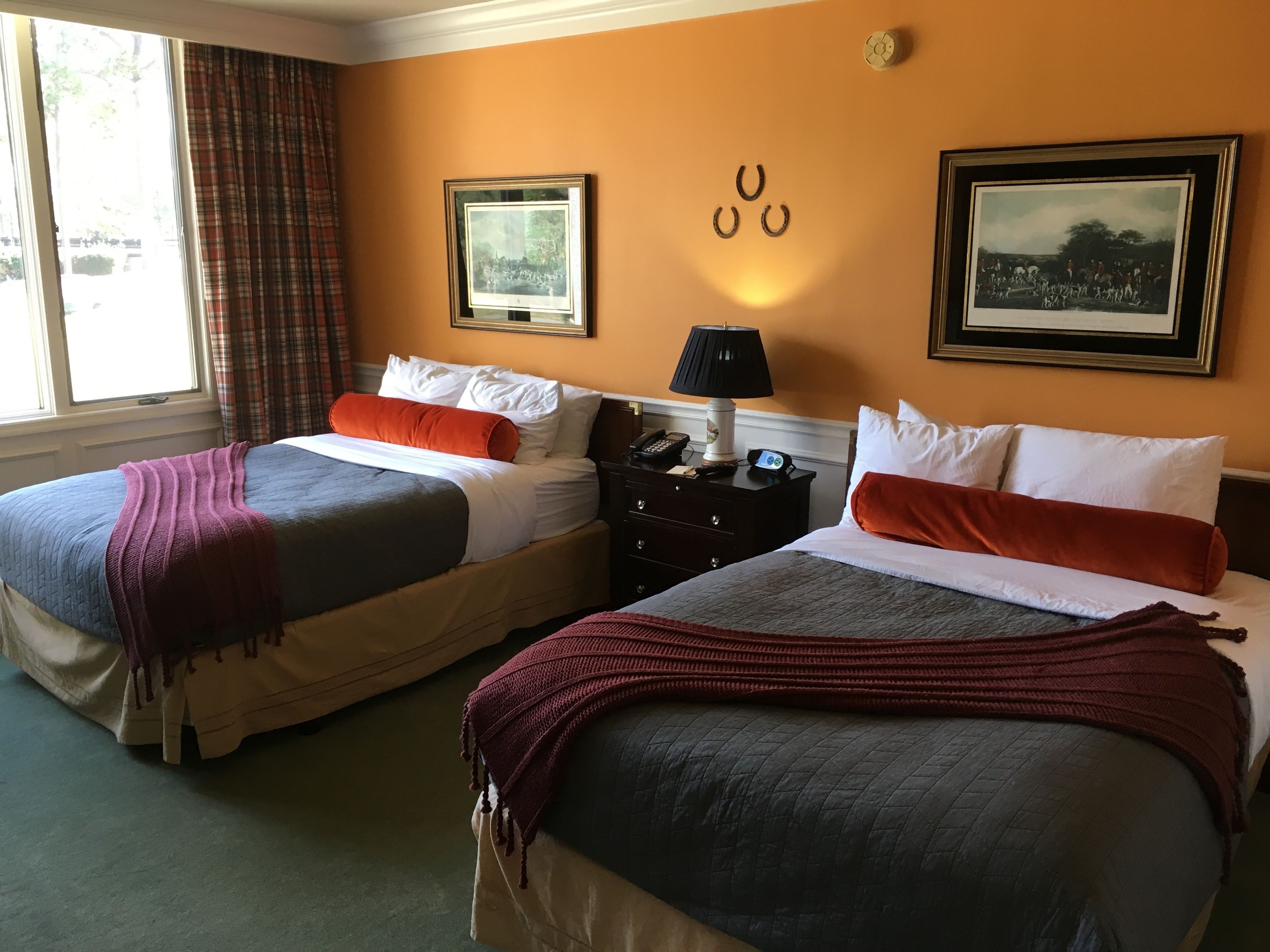 A hotel room with two beds, a nightstand with a lamp, and two framed pictures on the wall.