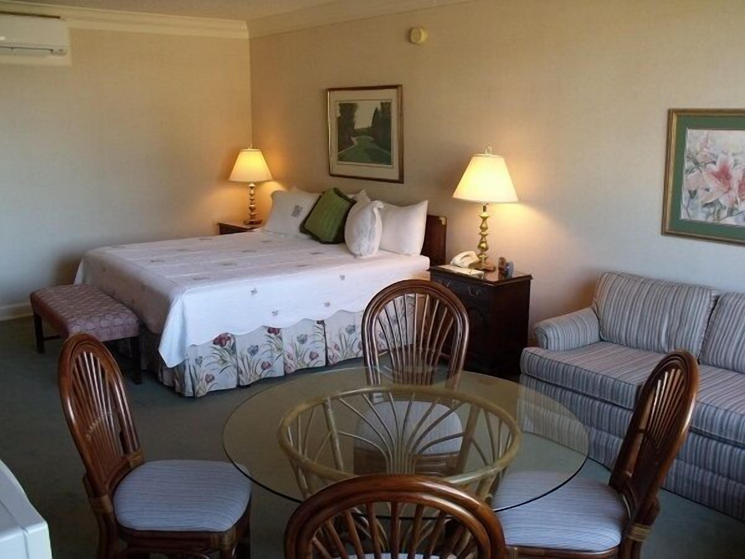 Une chambre d’hôtel comprenant un lit, deux lampes de chevet, un canapé, une table à manger avec des chaises et un tableau au mur.