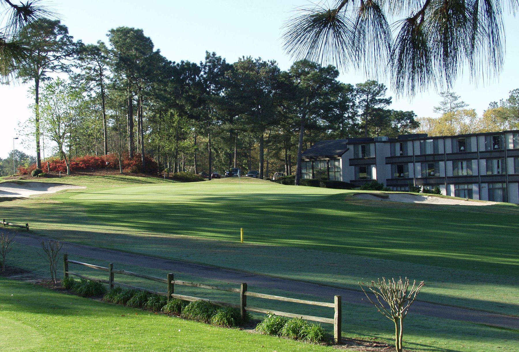 A golf course with a well-maintained green, a sand bunker, and a modern building with multiple windows and balconies.