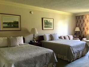 Une chambre d’hôtel avec deux lits, une table de chevet, une lampe et deux tableaux encadrés au mur.