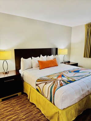 A hotel room with a large bed, two bedside tables with lamps, a nightstand, a wooden floor, and a window with curtains. - Surfsider Resort (Lauderdale-by-the-Sea)