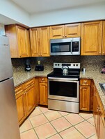A kitchen with wooden cabinets, a stainless steel refrigerator, a microwave, an oven, and a kettle.