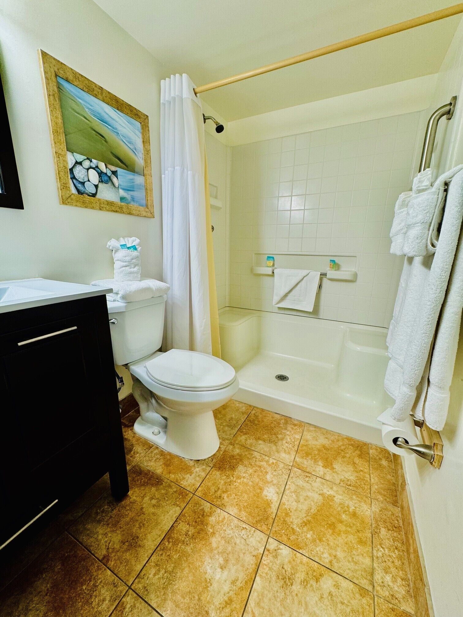 A bathroom with a toilet, a bathtub, and a shower. There is a towel rack with towels, a framed picture on the wall, and a sink with a mirror.