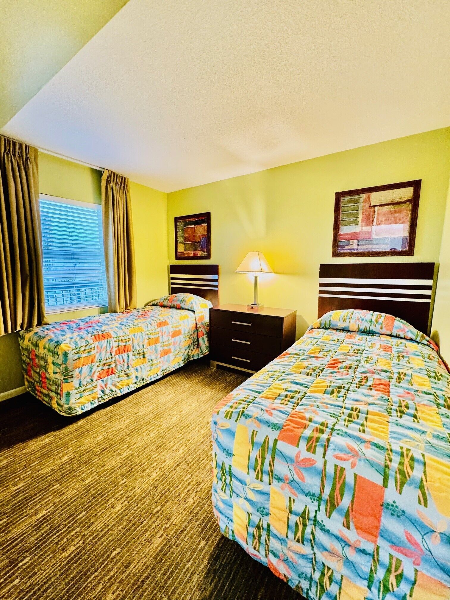 A hotel room with two beds, a nightstand, a lamp, and a window with curtains.