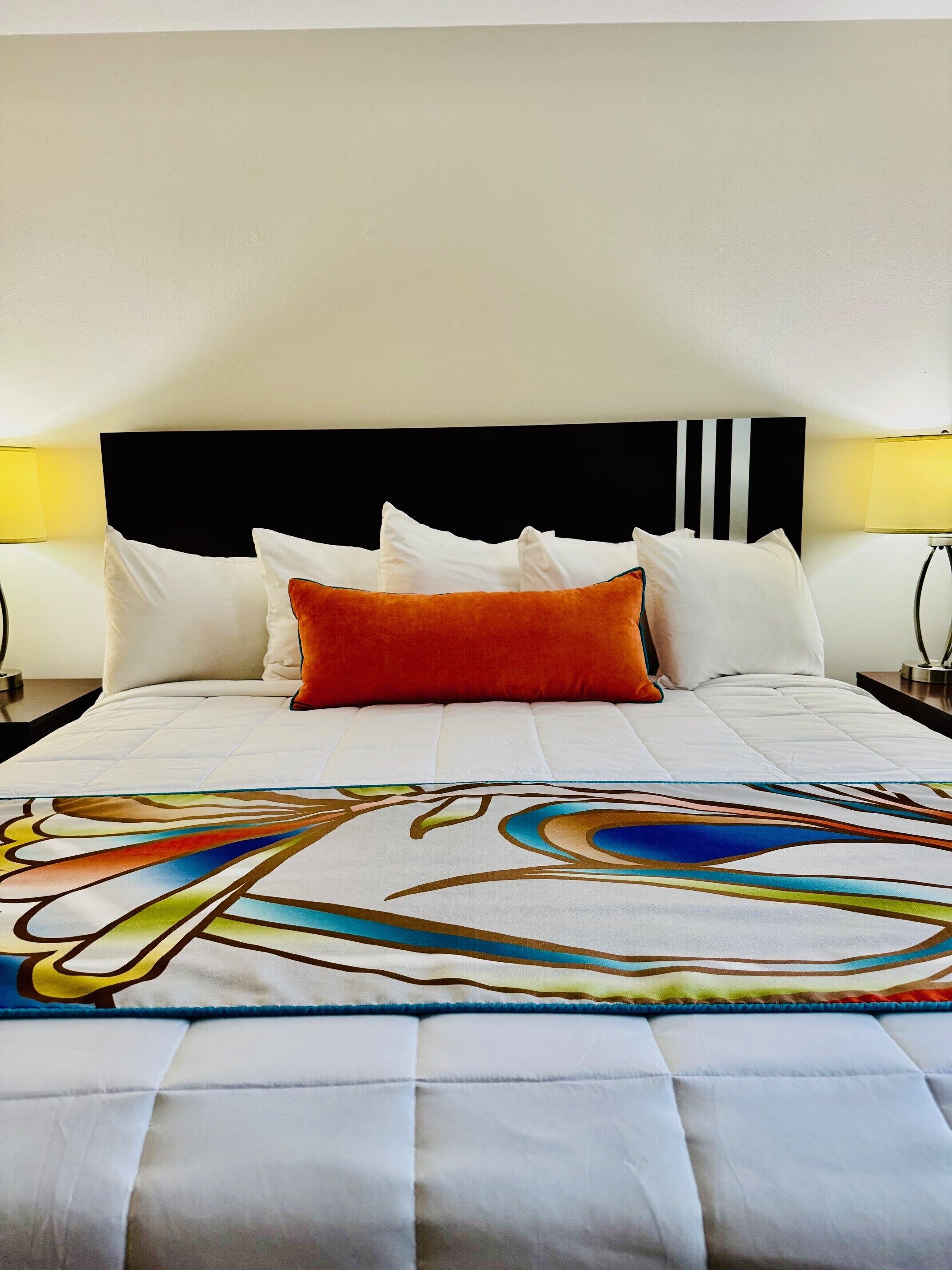 Une chambre d’hôtel avec un lit, du linge de lit blanc, une tête de lit noire et deux lampes de chevet.