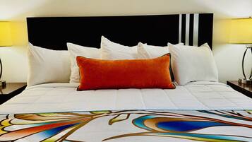 Una habitación de hotel con una cama, ropa de cama blanca, cabecera negra y dos lámparas de noche.