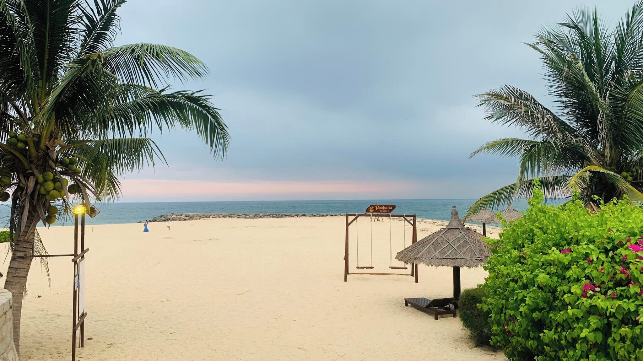 A beach with palm trees, a swing set, and a thatched-roof hut.