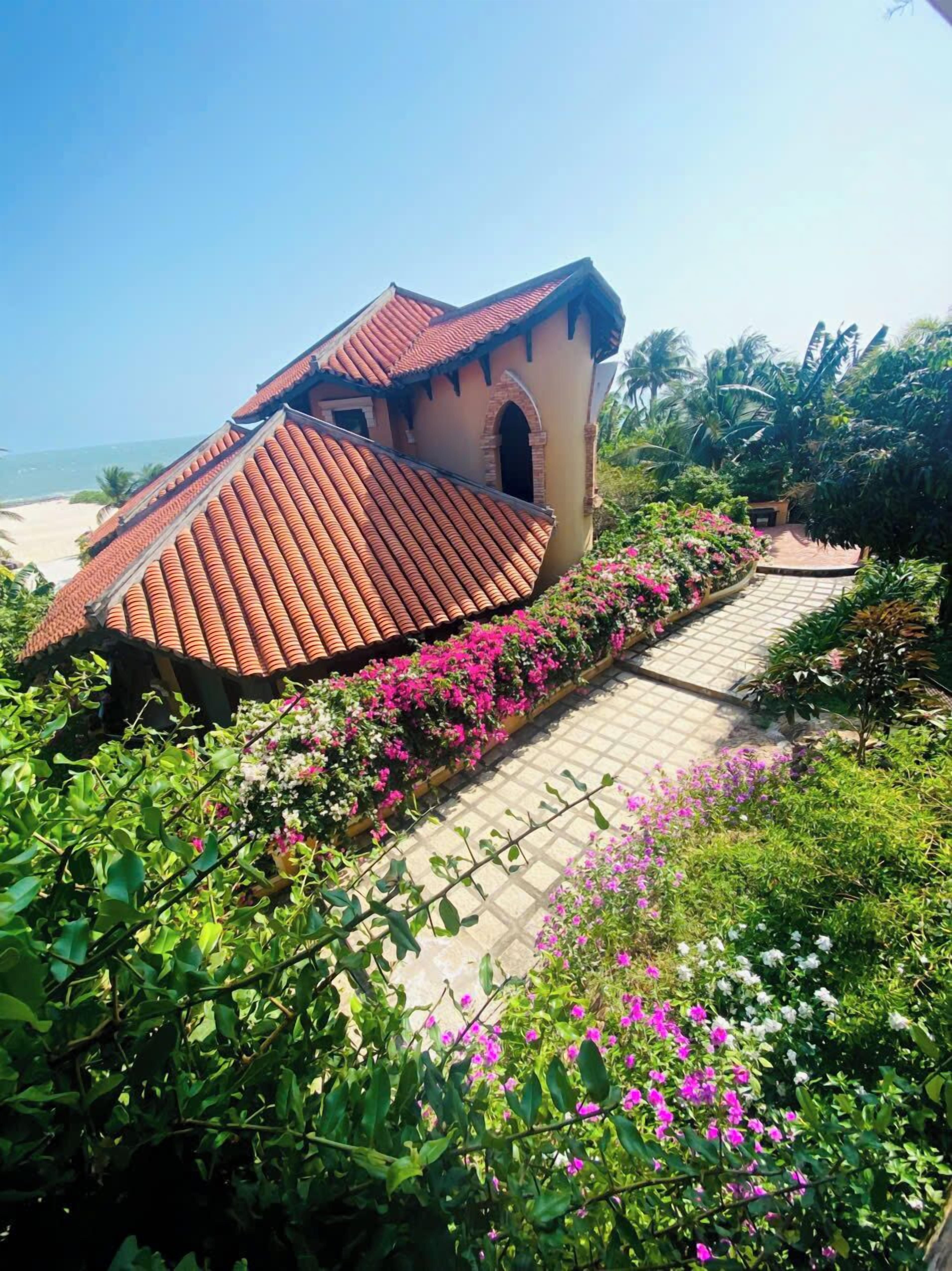 A building with a tiled roof, surrounded by lush greenery and flowers.