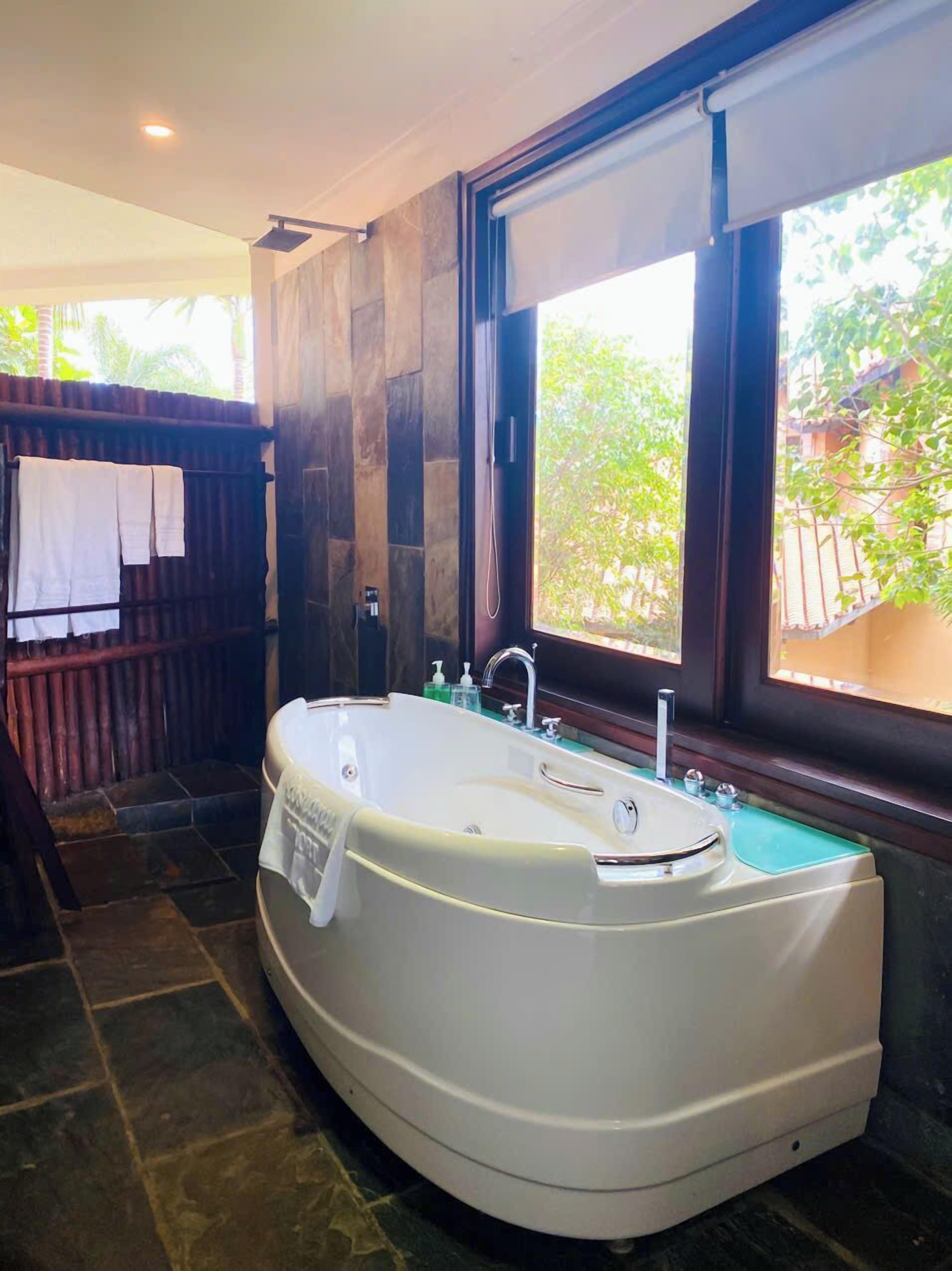 Un baño moderno con una bañera independiente, un ventanal con vista a la vegetación y un separador de madera.