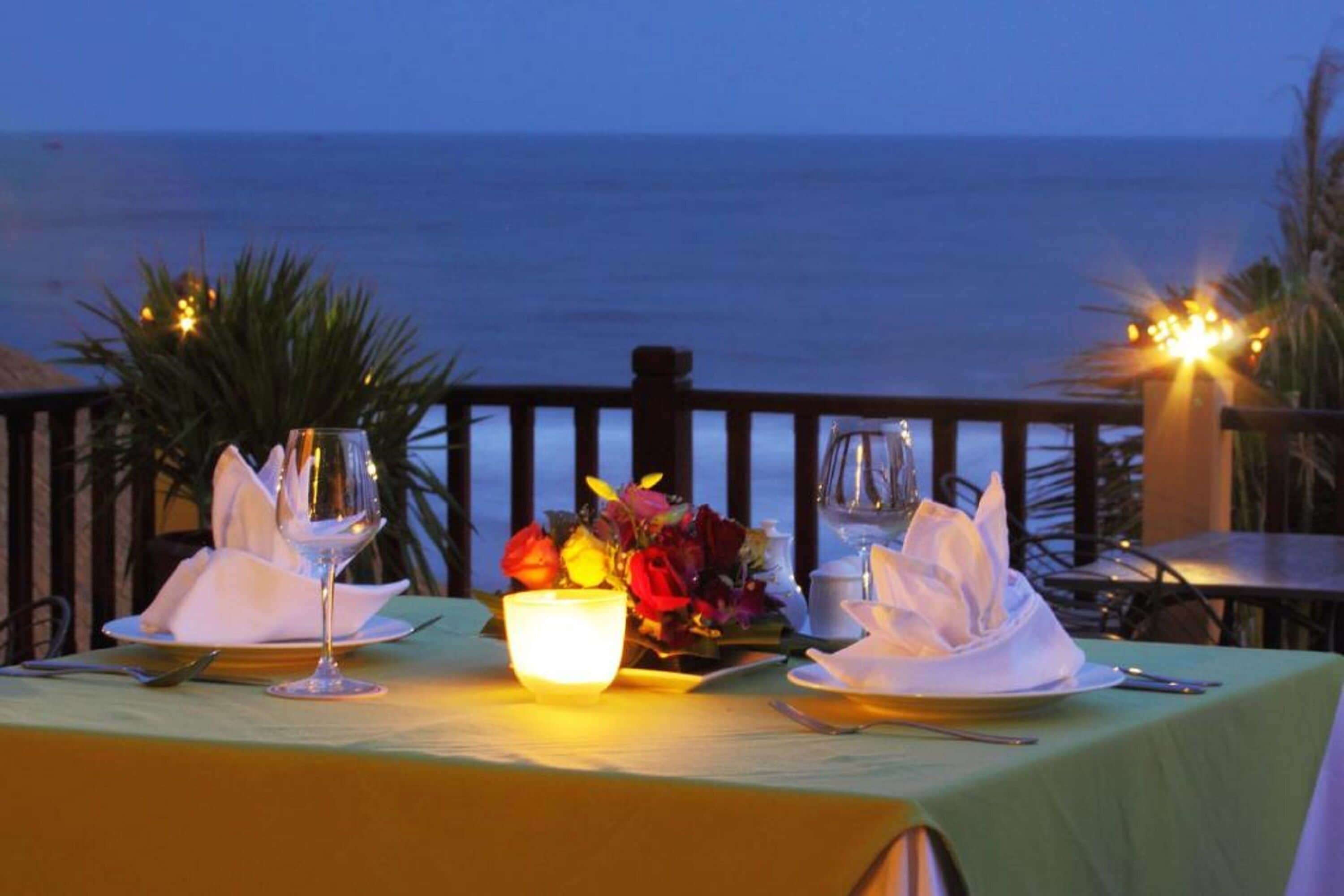 Una mesa para dos con vista al océano, una vela y un florero con flores.