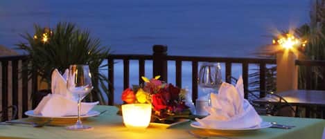 A table set for two with a view of the ocean, a candle, and a vase of flowers.