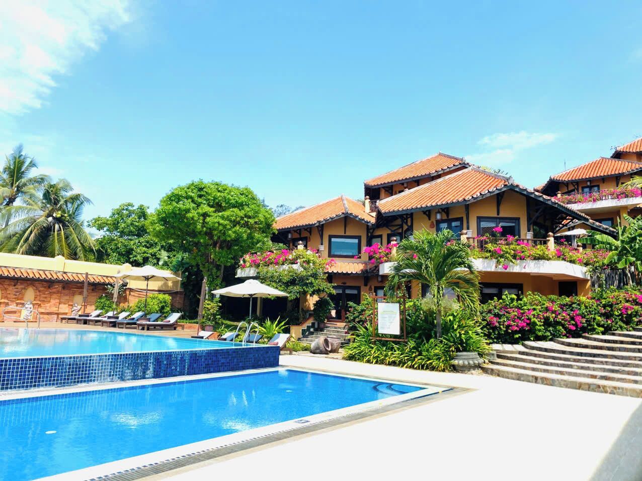 Un hôtel doté d’une piscine, de plusieurs balcons ornés de fleurs et d’un jardin tropical.