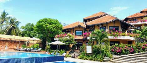Un hôtel doté d’une piscine, de plusieurs balcons ornés de fleurs et d’un jardin tropical.