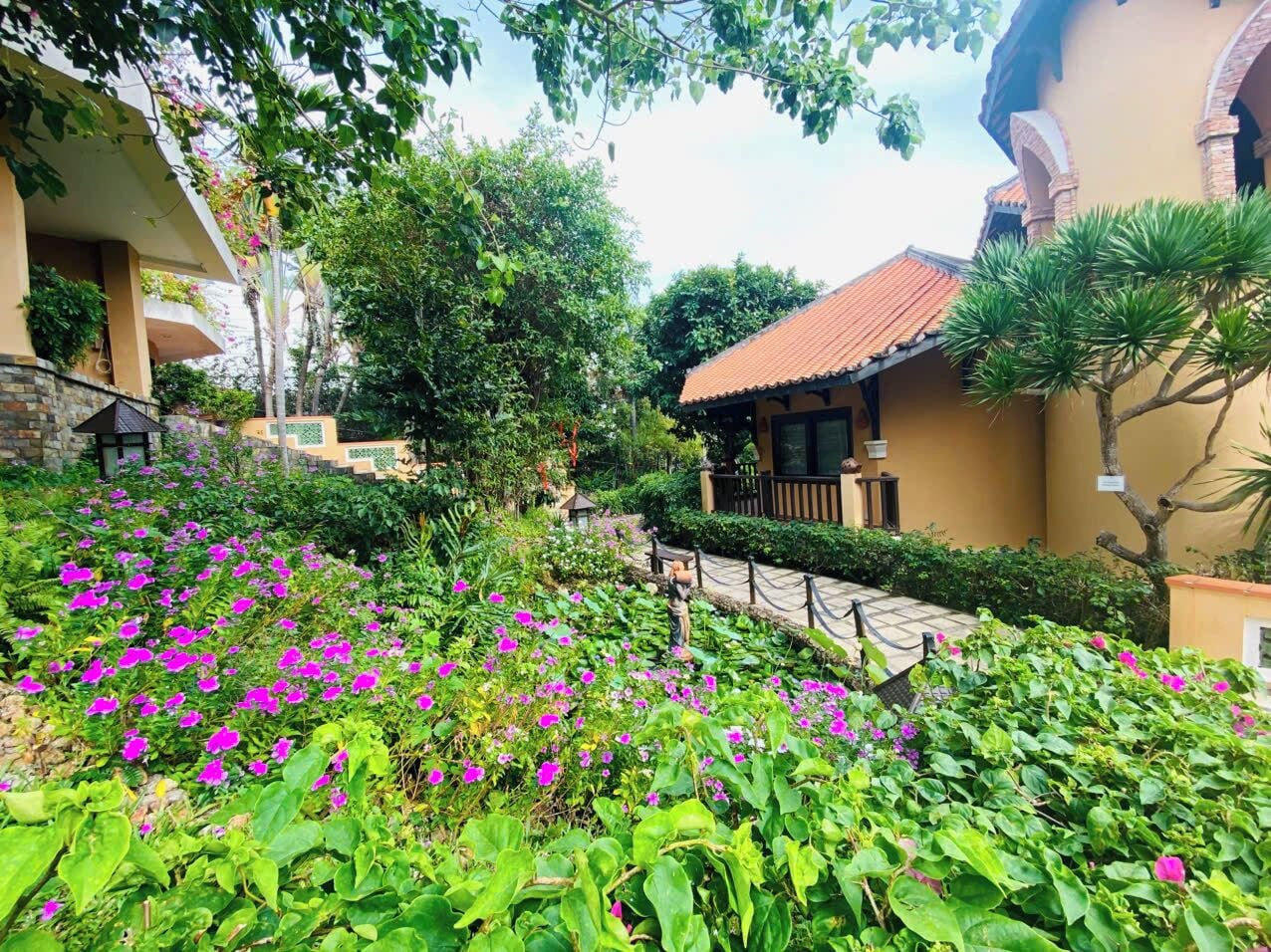 A garden with vibrant flowers, a pathway, and a building with a tiled roof.