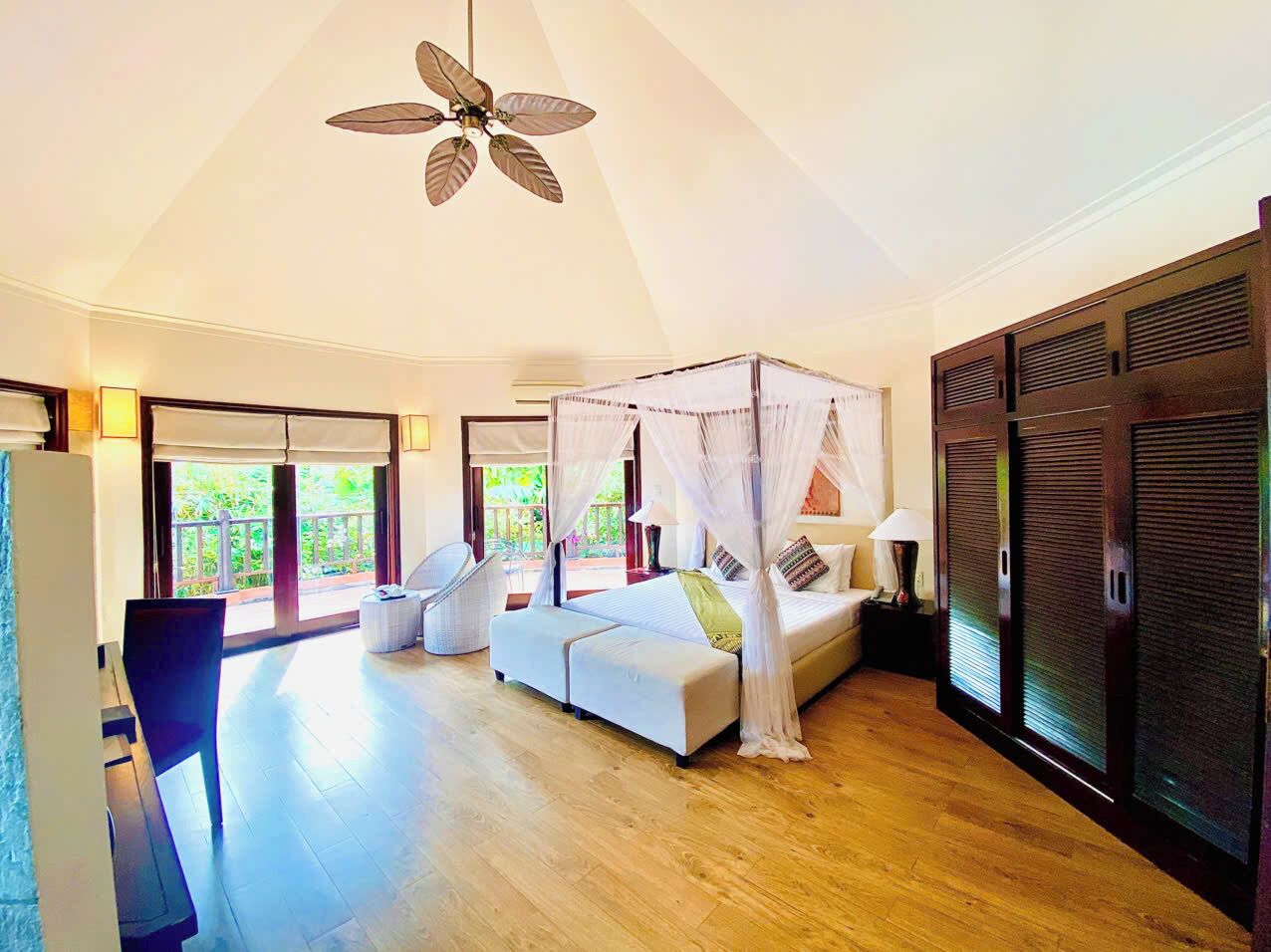 A spacious bedroom with a four-poster bed, a ceiling fan, and a view of the outdoors.