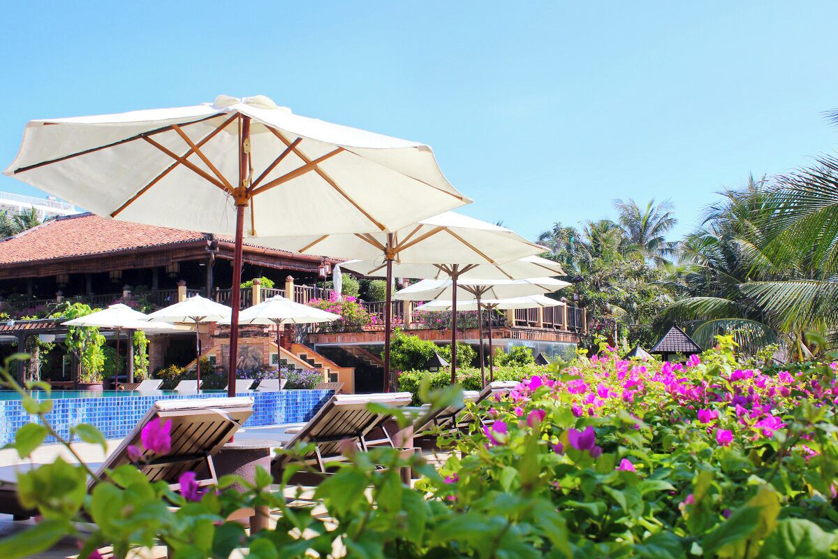 A pool area with lounge chairs and umbrellas, surrounded by lush greenery and flowers.