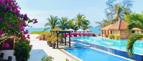 A resort pool area with a clear view of the ocean, surrounded by lush greenery and palm trees.